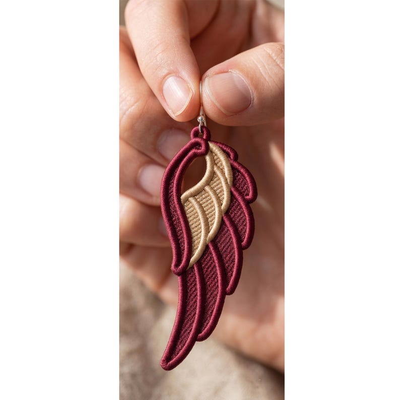 May include: A single wing-shaped earring featuring deep burgundy and metallic gold embroidery. The design consists of layered, curved segments with a prominent gold-colored inner section and a burgundy border, suspended from a silver-toned hook.