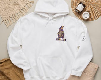 May include: A white hooded sweatshirt featuring a graphic of a gnome wearing a purple and gold checkered hat and outfit. Below the gnome, the text MINNESOTA is printed in purple and gold. The hoodie has a front kangaroo pocket and white drawstrings.