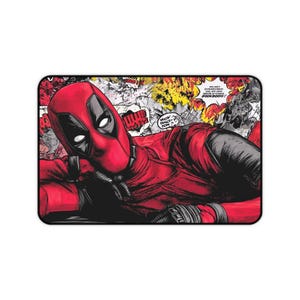 May include: A rectangular desk mat featuring a comic book style illustration of Deadpool in a red and black suit. The character is shown in a reclining pose against a background of yellow and white explosions with speech bubbles containing text.