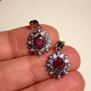 Puede incluir: Dos colgantes de plata con una piedra preciosa de rubí rojo rodeada de un diseño floral de pequeñas piedras preciosas blancas.