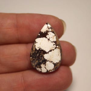 May include: A teardrop-shaped cabochon stone featuring a high-contrast pattern of creamy white sections interspersed with dark brown and black matrix veins. The polished surface has a smooth, rounded top and a distinct pear-like silhouette.