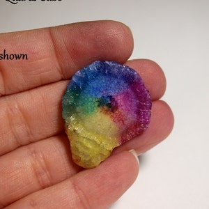 Puede incluir: Un cabujón de cuarzo arcoíris con un patrón en espiral. El cabujón es de color amarillo claro con un arcoíris de colores que irradian desde el centro.