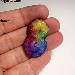 Puede incluir: Un cabujón de cuarzo arcoíris con un patrón de color amarillo, verde, azul, morado y rojo. El cabujón tiene aproximadamente el tamaño de una moneda de 25 centavos y tiene una superficie lisa y pulida.