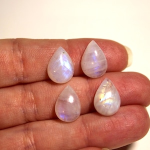 May include: Four teardrop-shaped moonstone cabochons with iridescent rainbow colors. The stones are white with a pearlescent sheen.