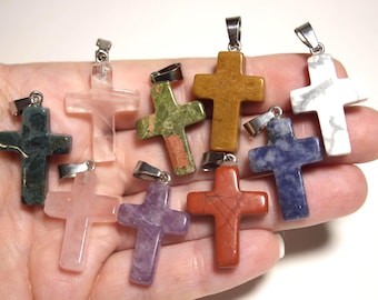 May include: A collection of nine cross-shaped pendants crafted from various polished gemstones, including rose quartz, green moss agate, unakite, yellow jasper, white howlite, blue sodalite, purple lepidolite, and red jasper, each with a silver-tone metal bail.