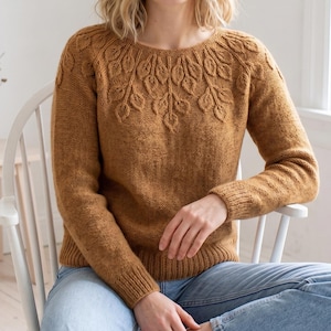 May include: A long-sleeved, mustard-yellow knit sweater featuring a round neckline and a textured leaf-pattern design radiating from the yoke. The garment has ribbed cuffs and a ribbed hem, showcasing a consistent stockinette stitch throughout.