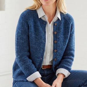 Könnte beinhalten: Blauer Strickcardigan mit strukturiertem Muster und Holzknöpfen. Der Cardigan ist zugeknöpft und wird über einem gestreiften Hemd getragen. Die Ärmel sind lang und die Passform ist locker.