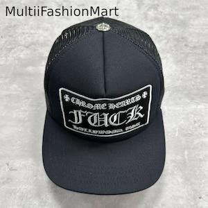 Puede incluir: Gorra de camionero negra con visera curva y parte trasera de malla. El panel frontal presenta un parche rectangular con el texto "CHROME HEARTS FUCK HOLLYWOOD USA" en blanco. Un pequeño emblema plateado en la parte superior.
