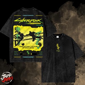Op de afbeelding: Een zwart acid-wash t-shirt met een grote gele afbeelding op de achterkant met de tekst Cyberpunk Edgerunners, I Really Want To Stay At Your House, en silhouetten van personages. De voorkant heeft een klein geel logo op de borst.