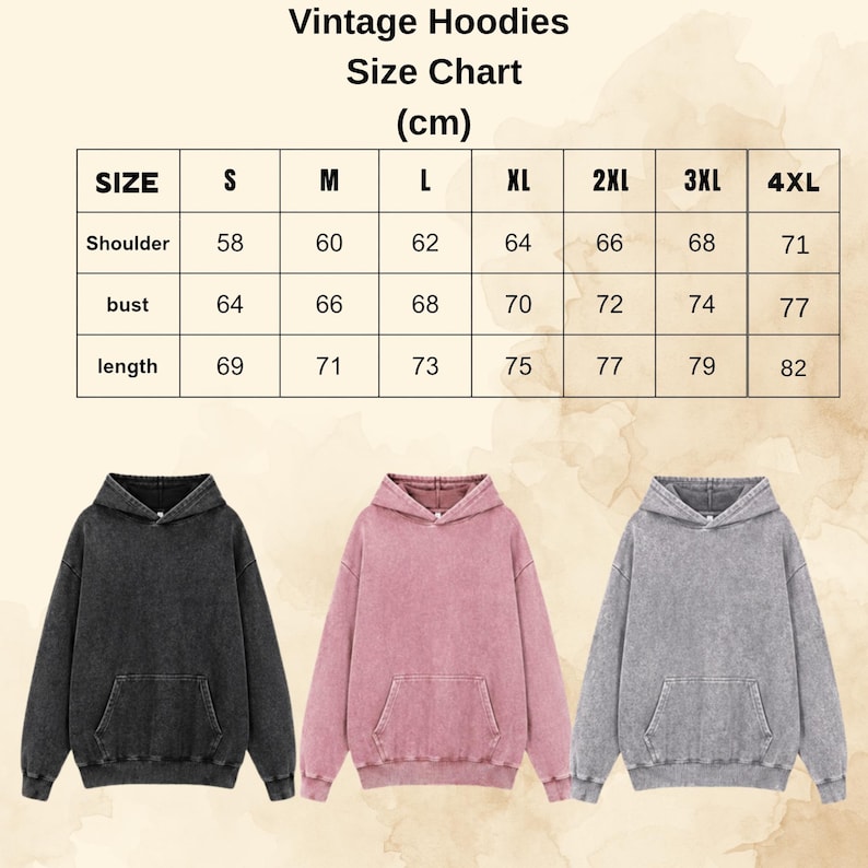 Op de afbeelding: Een maattabel voor vintage hoodies met afmetingen in centimeters voor maten S tot 4XL, inclusief schouder, borst en lengte. Onder de tabel staan drie hoodies met lange mouwen in zwart, oudroze en grijs met een gewassen afwerking.