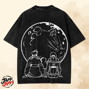 May include: A black acid-wash t-shirt featuring a large white circular graphic on the back. The design depicts two figures sitting and looking up at a detailed moon. The bottom left corner displays the text JAPY JAPY in a stylized black and red font.
