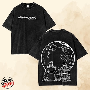 May include: A black acid-wash short-sleeve t-shirt featuring the white Cyberpunk 2077 logo on the front chest. The back of the shirt displays a large white graphic of two figures sitting and looking up at a detailed full moon in the night sky.