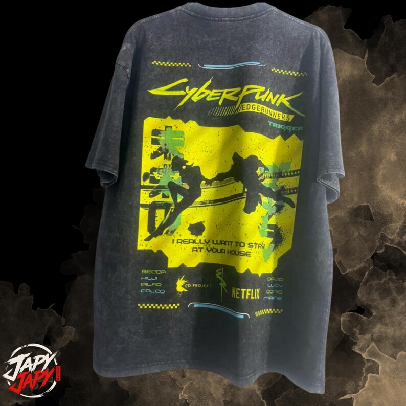 Op de afbeelding: Een antracietgrijs acid-wash t-shirt met een grote gele en groene afbeelding op de achterkant. Het ontwerp bevat de tekst Cyberpunk Edgerunners, I Really Want To Stay At Your House, Netflix en CD Projekt, samen met silhouetten van twee figuren.