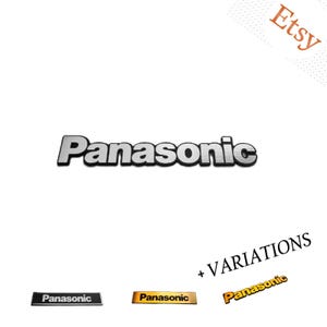May include: A silver Panasonic logo emblem with a black outline. Below are three variations: a black rectangular badge with white text, a gold rectangular badge with black text, and a gold-coloured Panasonic logo with a black outline.
