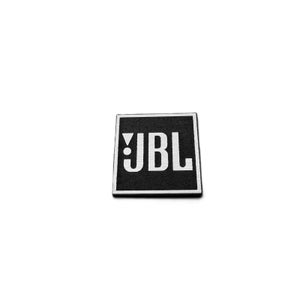 Peut inclure: Un patch carré noir avec les lettres blanches "JBL" en gras, sans empattement. Le patch a une bordure blanche et est posé sur un fond blanc uni. Le logo JBL est une marque bien connue.
