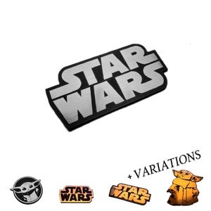 Op de afbeelding: Een zilverkleurig Star Wars logo-embleem met een zwarte rand. Hieronder staan extra items, waaronder een rond embleem met een karakterillustratie, twee kleinere Star Wars logo's in metallic afwerkingen en een figuur met de tekst + VARIATIONS.