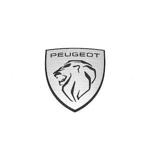 Może przedstawiać: Srebrzysty metalowy emblemat w kształcie tarczy ze szczotkowanym wykończeniem. Emblemat przedstawia czarny grawerowany profil głowy lwa skierowany w lewo oraz słowo PEUGEOT wydrukowane pogrubioną czcionką bezszeryfową w górnej części tarczy.