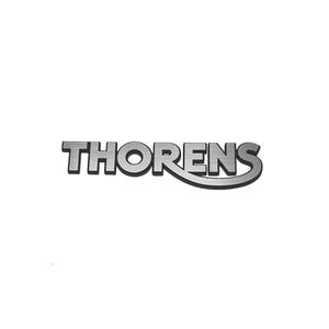 Könnte beinhalten: Ein silbernes Metall-Emblem mit dem Wort THORENS in einer fetten, serifenlosen Schriftart. Die Buchstaben haben eine gebürstete Oberfläche, und der untere Teil des Buchstabens S erstreckt sich in einer geschwungenen Linie unter R, E, N und S.