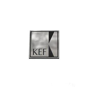 Könnte beinhalten: Ein quadratisches Metallemblem mit silberfarbenem Finish und schwarzem Rand. Die Buchstaben KEF sind in Schwarz auf der linken Seite aufgedruckt, während sich eine stilisierte schwarze Dreiecksform vom rechten Rand zur Mitte erstreckt.