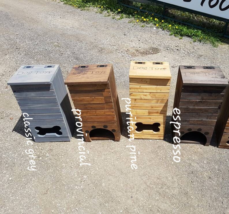 May include: Four wooden dog toy storage bins with different stain colors. The bins are labeled "Dog Toys" and have a bone-shaped opening. The colors are classic grey, provincial, puritan pine, and espresso.