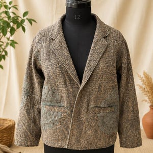 以下が含まれることがあります： 長袖、ノッチドラペル、セージグリーンの花柄刺繍パネル付きフロントポケット2つを備えた、ブラウンとタンのテクスチャード加工ブレザー。ジャケットは構造的なフィット感があり、織り生地には繊細なまだら模様が施されています。