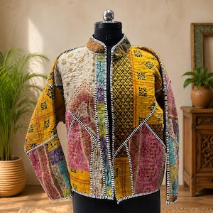 Pode incluir: Um casaco acolchoado com um design de patchwork de vários padrões florais e geométricos em tons de amarelo mostarda, rosa e creme. A peça tem uma gola mandarim e é rematada com debruns às riscas pretas e brancas nas costuras.