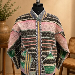 Puede incluir: Una chaqueta acolchada con diseño de patchwork que presenta bandas horizontales en negro, rosa, verde y amarillo. La prenda tiene cuello mao, mangas largas y una abertura frontal con detalles visibles de costura de festón en blanco y negro.