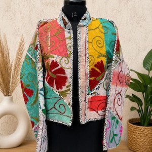 Op de afbeelding: Een kleurrijke patchworkjas met een opstaande kraag. De jas heeft verschillende stoffen in roze, teal, geel en rood, met bloemen- en krulborduurwerk. De randen zijn afgewerkt met witte stiksels.