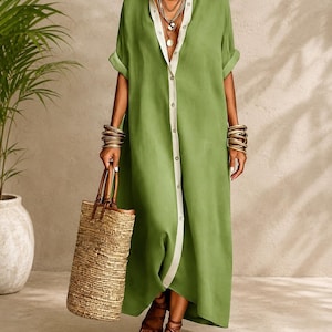 Puede incluir: Vestido largo verde oliva con botones, ribete blanco y mangas enrolladas. El conjunto incluye un bolso tote tejido con asas de cuero marrón y sandalias. La persona lleva pulseras y collares dorados.