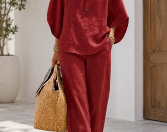 May include: A red linen two-piece outfit featuring a mandarin collar top with button details and wide-leg pants. The outfit is paired with a woven straw tote bag. The ensemble is a casual, yet stylish, summer outfit.