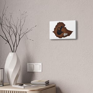May include: A rectangular wall art piece featuring a brown silhouette of the map of Ethiopia. Centered on the map is a black traditional coffee pot, known as a jebena, accompanied by three small white coffee cups arranged in a cluster.