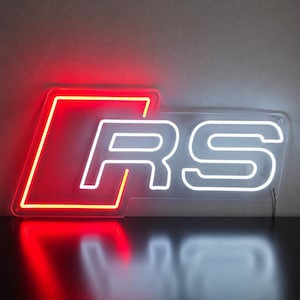 May include: A neon sign featuring a red parallelogram outline on the left side and the white letters RS on the right side. The sign is mounted on a clear acrylic backing and emits a bright glow, creating a reflection on the surface below.
