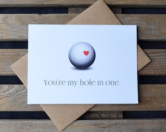 May include: A white golf ball with a red heart on it. The card reads "You're my hole in one."