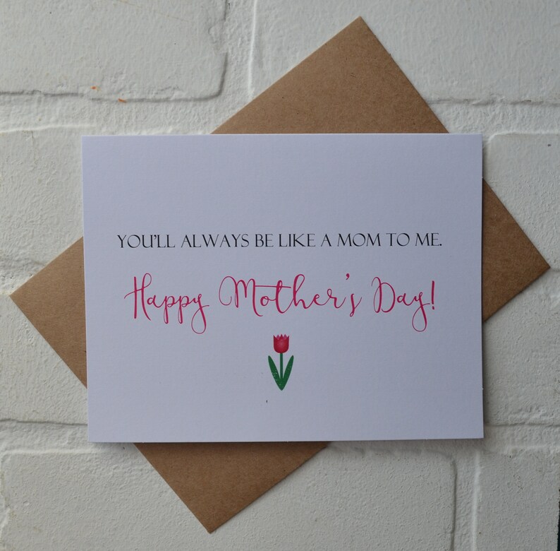 Może przedstawiać: Biała kartka z tekstem "You'll always be like a mom to me. Happy Mother's Day!" w r&oacute;żowym, ozdobnym piśmie. Pod tekstem znajduje się r&oacute;żowy tulipan z zieloną łodygą i liśćmi.