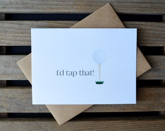 May include: A white card with a golf ball on a tee and the text "I'd tap that!" printed on it. The card is sitting on a brown envelope.