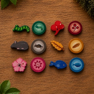 May include: A collection of twelve small wooden game tokens arranged in a grid. The set includes six shaped pieces depicting a green caterpillar, a gray mouse, a pink flower, a red berry cluster, a yellow leaf, and a blue fish, alongside six matching circular discs.