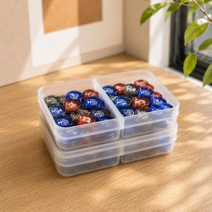 May include: A clear plastic rectangular storage container with a central divider, filled with numerous small, round, translucent game tokens in shades of blue, red, and black. Each token features a white printed number three on its surface.