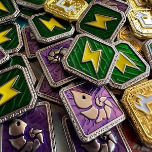 May include: A collection of square metal tokens featuring raised silver borders. Some tokens display a yellow lightning bolt on a green background, others show a silver nautilus-like shell on a purple background, and some feature a white symbol on a gold background.