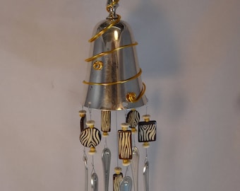 May include: A silver wind chime with a metal cup at the top and a gold wire design. The chime has multiple forks and spoons hanging from it, with black and white zebra print beads.