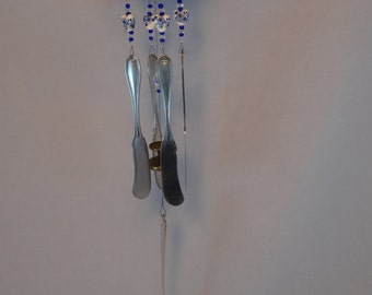 May include: A silver wind chime with blue and white beads and a silver top. The chime has four silver spoons hanging from it.
