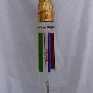 May include: A gold-colored wind chime made from a repurposed wine glass with a copper wire design. The chime has six hanging pieces of colored glass, including green, red, blue, and yellow. A silver serving spoon hangs from the bottom.
