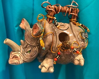 May include: A ceramic rhino birdhouse with a hanging chain, decorated with beads, feathers, and a zebra-patterned handle.