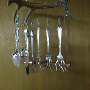 May include: A wind chime made from a deer antler, copper pipe, and silverware. The chime features turquoise beads and hangs from a chain.