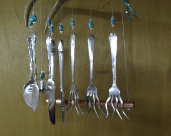 May include: A wind chime made from a deer antler, copper pipe, and silverware. The chime features turquoise beads and hangs from a chain.