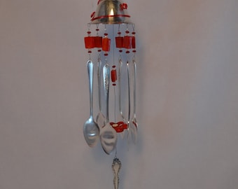 May include: A silver wind chime made from spoons and red glass beads hangs from a silver goblet. The wind chime is suspended from the ceiling.