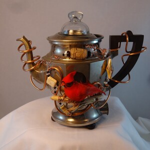 Könnte beinhalten: Eine Kaffeekanne aus Silber und Kupfer mit einem Glasdeckel, verziert mit einem roten Kardinal, Perlen und anderen Verzierungen.