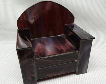 May include: A small, purple glass armchair with a black metal frame. The chair has a curved back and a seat with a swirling pattern.