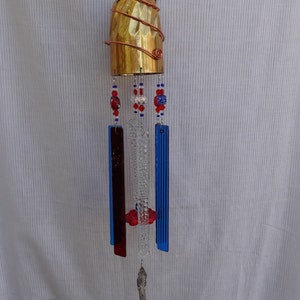 May include: A wind chime made from a brass goblet, with red, white, and blue glass beads and glass panels, and a silver spoon hanging from the bottom.
