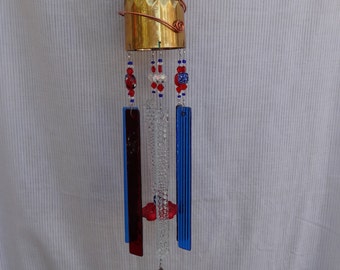 May include: A wind chime made from a brass goblet, with red, white, and blue glass beads and glass panels, and a silver spoon hanging from the bottom.