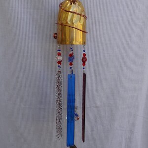 May include: A gold wind chime with a spoon, glass beads, and glass panels hanging from a brass goblet. The beads are red, blue, and white.